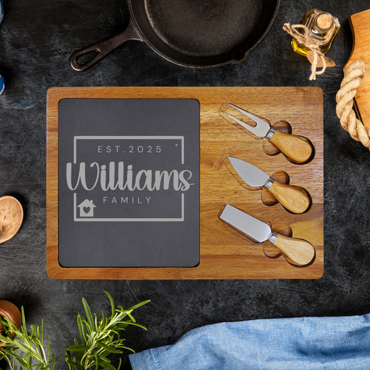 Wooden cutting board with personalized design, cheese knives, and a skillet on a dark surface.