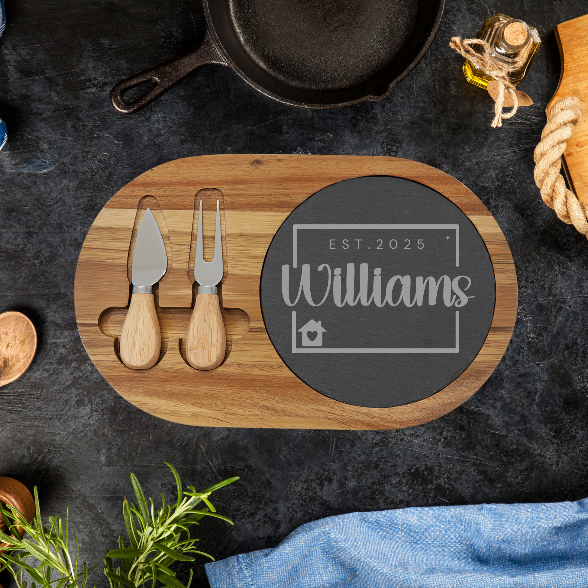 Wooden cutting board with cheese tools and personalized chalkboard sign on a dark surface.