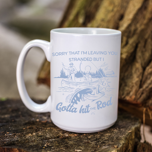 15oz white ceramic coffee mug with a blue design of a fisherman in a lake fishing a wild fish and the funny phrase "sorry that i'm leaving you stranded but I gotta hit the rod"